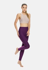 Lila Leggings mit hohem Bund und glatter Textur, kombiniert mit einem nahtlosen Sport-BH in hellbeige, beide für den aktiven Einsatz konzipiert.