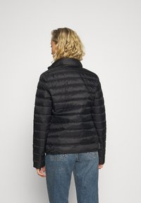 Svart dunjacka med hög krage och horisontella quiltade paneler. Bärs över ljusblå denimjeans. Mjuk textur.