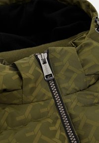 Olive green puffer jacket with a geometric pattern, featuring a silver zipper and black inner lining. Accented with ribbed hem.