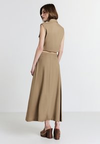 Set composto da un gilet corto beige e una lunga gonna. Tessuto testurizzato con una leggera lucentezza. La gonna presenta una spacco laterale. Scarpe con zeppa marroni con dettagli in metallo.