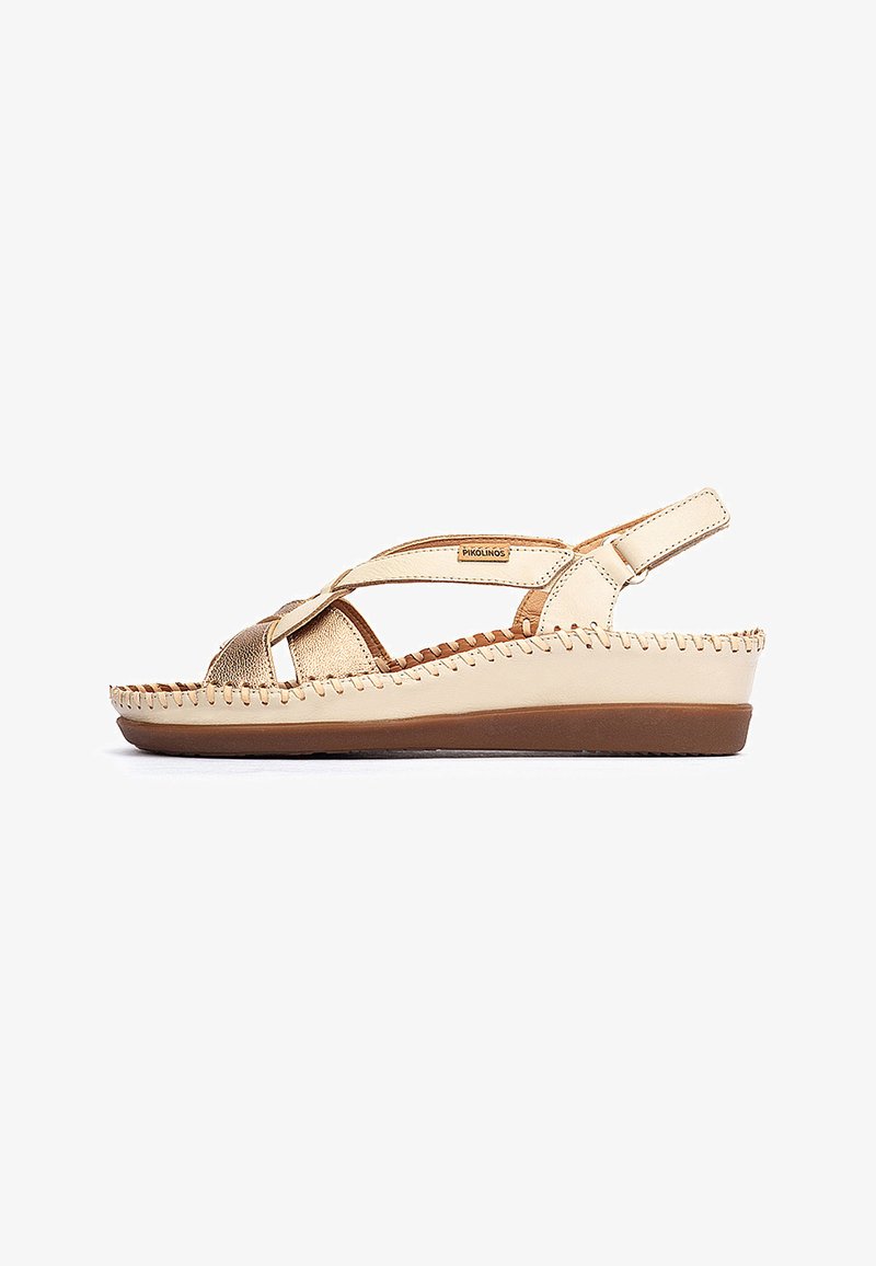Sandales beige clair avec une bride métallique et des détails cousus, dotées d'une semelle plate et d'une bride arrière réglable pour un maintien sûr.