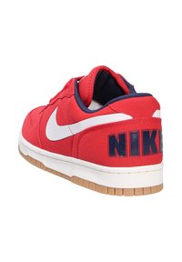 Zapatilla roja con el logo de Nike en blanco, detalles en azul marino, parte superior de textil, cuello acolchado y suela de goma. "NIKE" impreso en el talón.