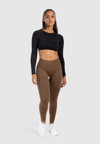 Czarny, długi rękaw crop top połączony z wysokimi brązowymi legginsami, o gładkiej fakturze i dopasowanym kroju, uzupełniony białymi sneakersami.