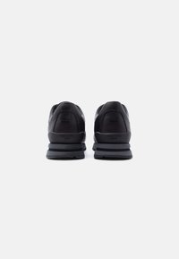 Paire de baskets de sport noires avec des semelles épaisses grises, vues de dos sur un fond blanc.