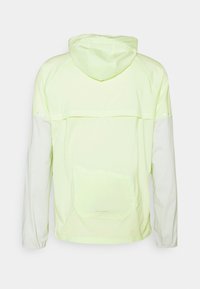 Chaqueta con capucha verde claro, de mangas largas, puños elásticos, bolsillo trasero y detalles reflectantes en la parte superior de la espalda y en los brazos.