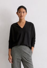Schwarzer V-Ausschnitt-Pullover aus weichem Stoff, mit langen Ärmeln und lockerer Passform, kombiniert mit grauen strukturierten Hosen.