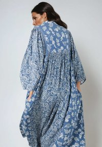 Blauwe jurk met een patroon, gemaakt van lichte stof, met lange mouwen, een geplooide rug, bloemmotieven en zakken.