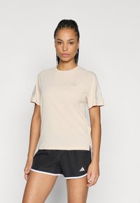 Ανοιχτό ροζ αθλητική μπλούζα με κοντά μανίκια, στρογγυλή λαιμόκοψη και μικρό λογότυπο στο στήθος. Συνδυάζεται με μαύρα αθλητικά σορτς με λευκές λεπτομέρειες.