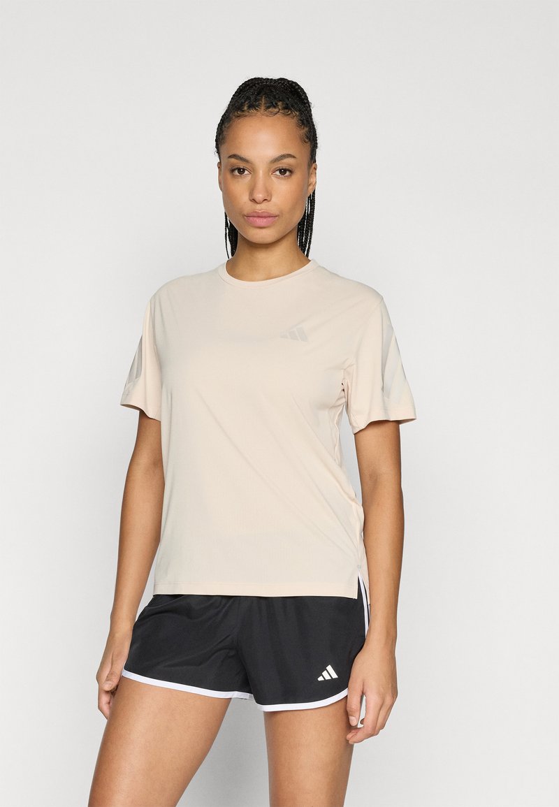 Ανοιχτό ροζ αθλητική μπλούζα με κοντά μανίκια, στρογγυλή λαιμόκοψη και μικρό λογότυπο στο στήθος. Συνδυάζεται με μαύρα αθλητικά σορτς με λευκές λεπτομέρειες.