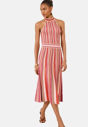 Kobieta w sukience midi bez rękawów z dekoltem halter i pionowymi paskami w kolorach różowym, czerwonym i beżowym, uzupełniona kolczykami i bransoletką.