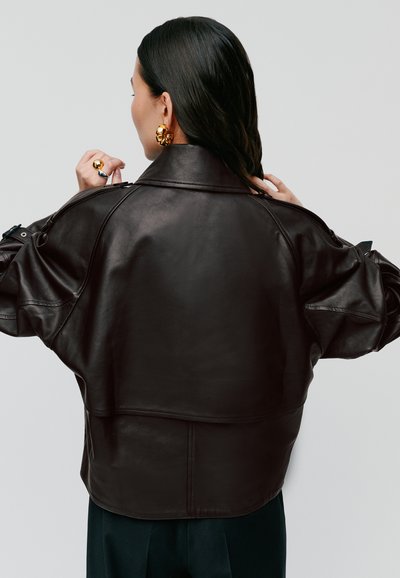 Braune Lederjacke mit einem taillierten Design, weiten Ärmeln und hohem Kragen. Auffällige glatte Textur und minimalistischer Stil.