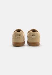 Tan-farbene Wildledersneaker mit niedrigem Profil, abgerundetem Absatz, strukturiertem Innenfutter und Gummisohle, die auf der Rückseite mit einem eingestempelten Logo versehen ist.