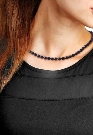 Collier en perles bleues avec des perles en forme d'ovale, porté autour du cou, contrastant avec un haut noir légèrement brillant.