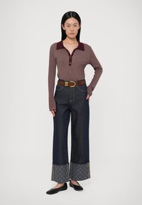 Vilkt ceriņu krāsas adītu topu ar apkakli un pogām, kopā ar tumšām platajiem džinsiem ar rakstainiem aprocēm un brūnu jostu. Melni dzīvokļi.