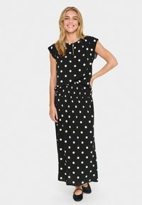Robe maxi noire à pois avec des manches courtes volantées et une taille froncée, présentant un col rond et une texture de tissu lisse.