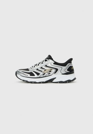 Baskets de sport Skechers noires et argentées avec semelle intermédiaire blanche, semelle texturée, design à lacets, et détails de marque sur le côté et le talon.