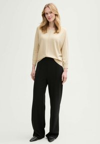 Beige leichter Pullover mit Rundhalsausschnitt und subtiler Stickerei, kombiniert mit hoch taillierten schwarzen Weitbein-Hosen und spitzen schwarzen Schuhen.