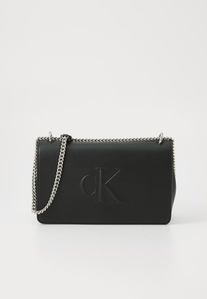 Bolso de mano de cuero negro con logotipo "cK" en relieve, cadena plateada y forma rectangular elegante. Textura suave con hardware minimalista.