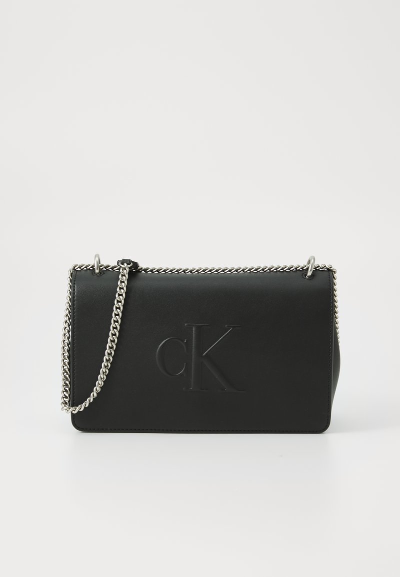 Borsa a mano in pelle nera con logo "cK" in rilievo, tracolla in catena argentata e forma rettangolare elegante. Texture liscia con hardware minimal.