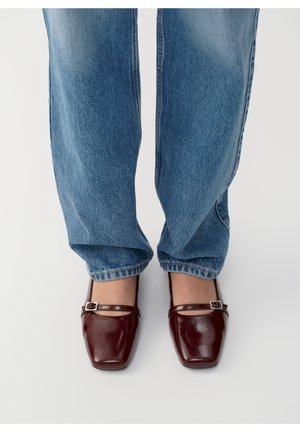 Burgundy patent leather Mary Jane shoes with square toes and a narrow strap. Worn with relaxed fit blue denim jeans.