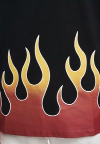 Melnas auduma T-krekls ar liesmu dizainu dzeltenā uz sarkanu gradientā apakšā, ar baltām kontūrām ap liesmām.