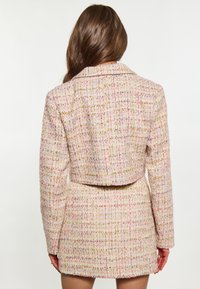 Giacca cropped in tweed rosa e giallo con colletto strutturato, tessuto texturizzato e silhouette aderente, abbinata a una gonna coordinata.