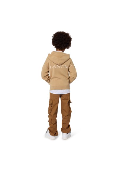 Felpa beige con cappuccio con logo "LANVIN" sul retro, abbinata a pantaloni cargo marroni con tasche laterali. Sneakers bianche completano il look.