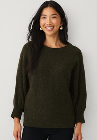 Pull en maille vert olive avec un col rond et des manches larges trois-quarts. Texture douce avec ourlet et poignets côtelés.