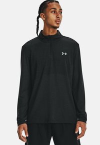 Sort langærmet trøje med halvdelslynlås og svedtransporterende stof, struktureret mønster og grå Under Armour-logo på brystet.