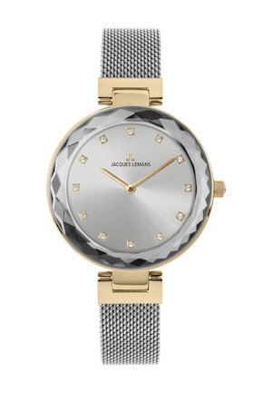 Rund silverklocka med fasetterad kristall, guldackenter, silvernätarmband, minimalistiska timmarkörer och varumärkeslogotyp i centrum.