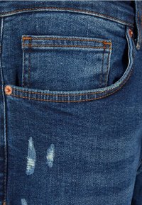 Jean en denim de couleur bleu foncé, avec un léger effet de délavage, des détails effilochés et un design classique de poche arrière avec des rivets en cuivre.