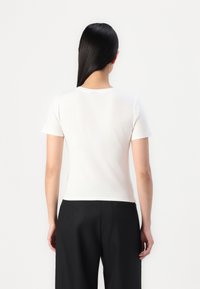 T-shirt blanc à manches courtes en tissu lisse, avec un col ras du cou et une coupe ajustée, associé à un pantalon noir.