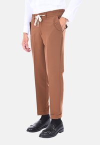 Pantaloni marroni a sigaretta con vita elastica, coulisse bianca, tasche a toppa e dettagli a contrasto con pieghe lungo i lati.