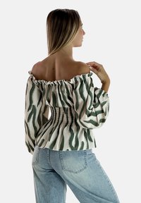 Blusa off-the-shoulder color crema con motivi a ondulazione verde, dotata di maniche a sbuffo e vita arricciata per una silhouette aderente.