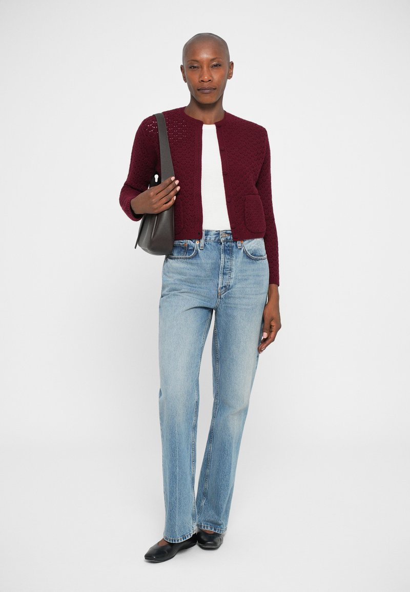Bordeaux strikket cardigan med rund hals, knaplukning og forlommer, parret med lysblå flagrende jeans og sorte sko.