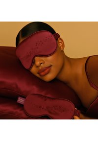 Maschera per dormire in raso bordeaux con motivo a punti in rilievo, abbinata a cuscino in raso coordinato, superficie strutturata e morbido elastico.