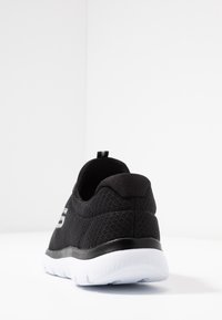 Svart nät sneaker med en texturerad ovandel, dragflik och en kontrasterande vit sula. Har en slät svart accent vid hälen.