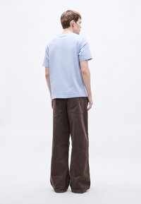 Svetlomodré tričko s krátkym rukávom a hnedé široké nohavice s voľným strihom a dvoma zadnými vreckami. Hladká textúra látky po celom povrchu.