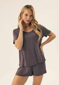 Purple loungewear set featuring a short-sleeve, V-neck top and matching shorts. Soft fabric with a relaxed fit and layered design.