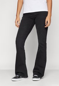 Sorte flared denim jeans med en glatt tekstur, tettsittende over livet og lårene, som flareer fra kneet til kanten. Brukt med sorte sneakers.