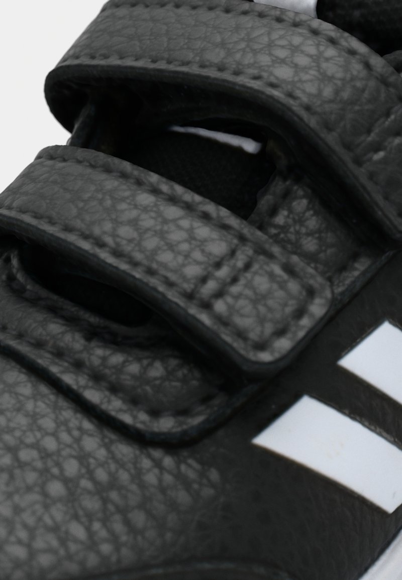 Nahaufnahme eines schwarzen, strukturierten Ledersneakers mit verstellbaren Klettverschlüssen und weißen Streifen an der Seite.