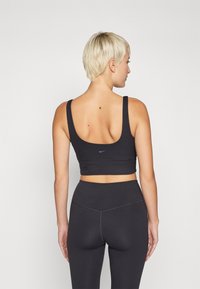 Sutien desportivo preto com nervuras, com alças largas, design cropped, logotipo discreto da Nike nas costas, combinado com leggings pretas de cintura alta.