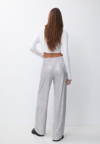 Zilveren wijde broek met een glanzende textuur en een elastische tailleband, gecombineerd met een aansluitend wit lange mouwen top.
