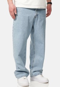 Light blue denim jeans with a loose fit, straight legs, and a subtle texture. Worn with white sneakers, showing a relaxed style.
