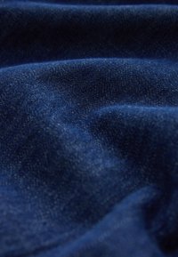 Tissu texturé bleu foncé avec tissage visible et plis doux créant des ombres et des reflets délicats.