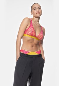 Rosa spets-bh med en gul underband, i kombination med högmidjade mörkgrå byxor. Har en intrikat spetsdesign och en smickrande passform.