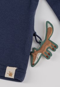 Marineblaues Sweater-Gewebe mit strukturiertem Finish, versehen mit einem braunen und grünen, fuchsförmigen Etikett, das am Ärmelabschluss befestigt ist.