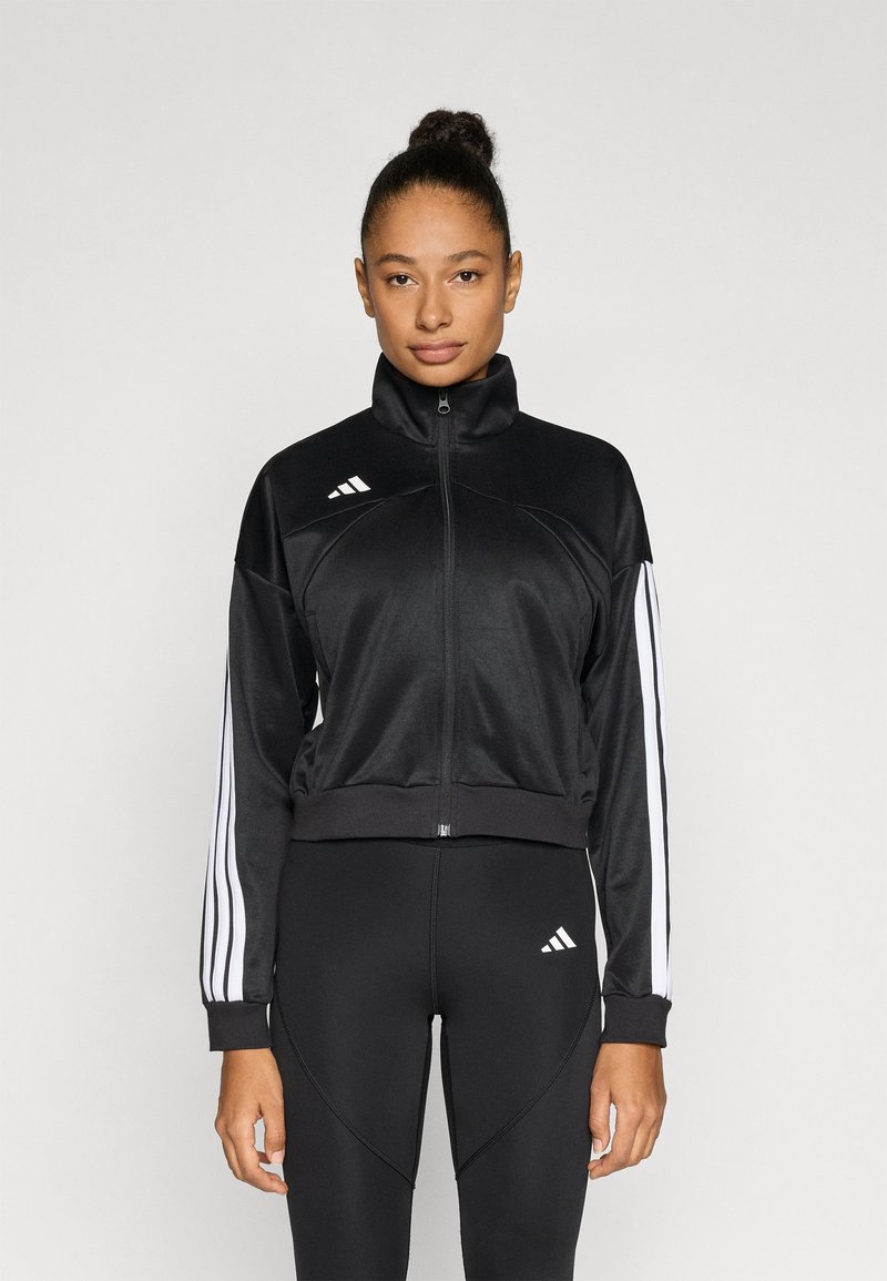 Črna športna jakna iz gladkega blaga, z visokim ovratnikom, zadrgo po celotni dolžini in belimi tremi črtami na rokavih.