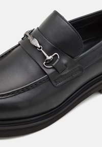 Melnas ādas slip-on loafer tipa kurpes ar gludu faktūru, apaļu purngalu, dekoratīvu siksniņu ar sudraba krāsas aksesuāru.