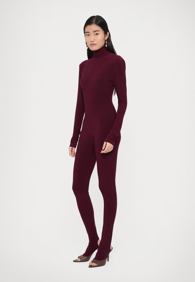 Bordový priliehavý overal s dlhými rukávmi a vysokým golierom. Hladká textúra bez viditeľných vzorov. Kombinovaný s hnedými otvorenými lodičkami.